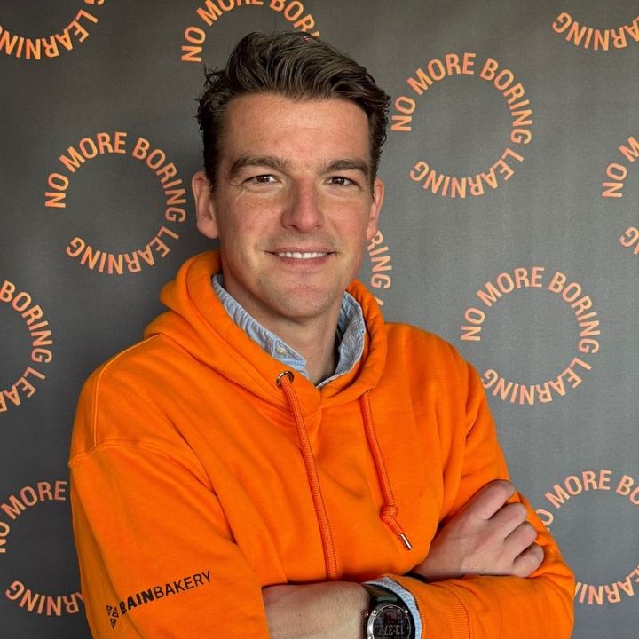 Bas Diepeveen in een oranje Brain Bakery-hoodie voor een wand met No More Boring Learning